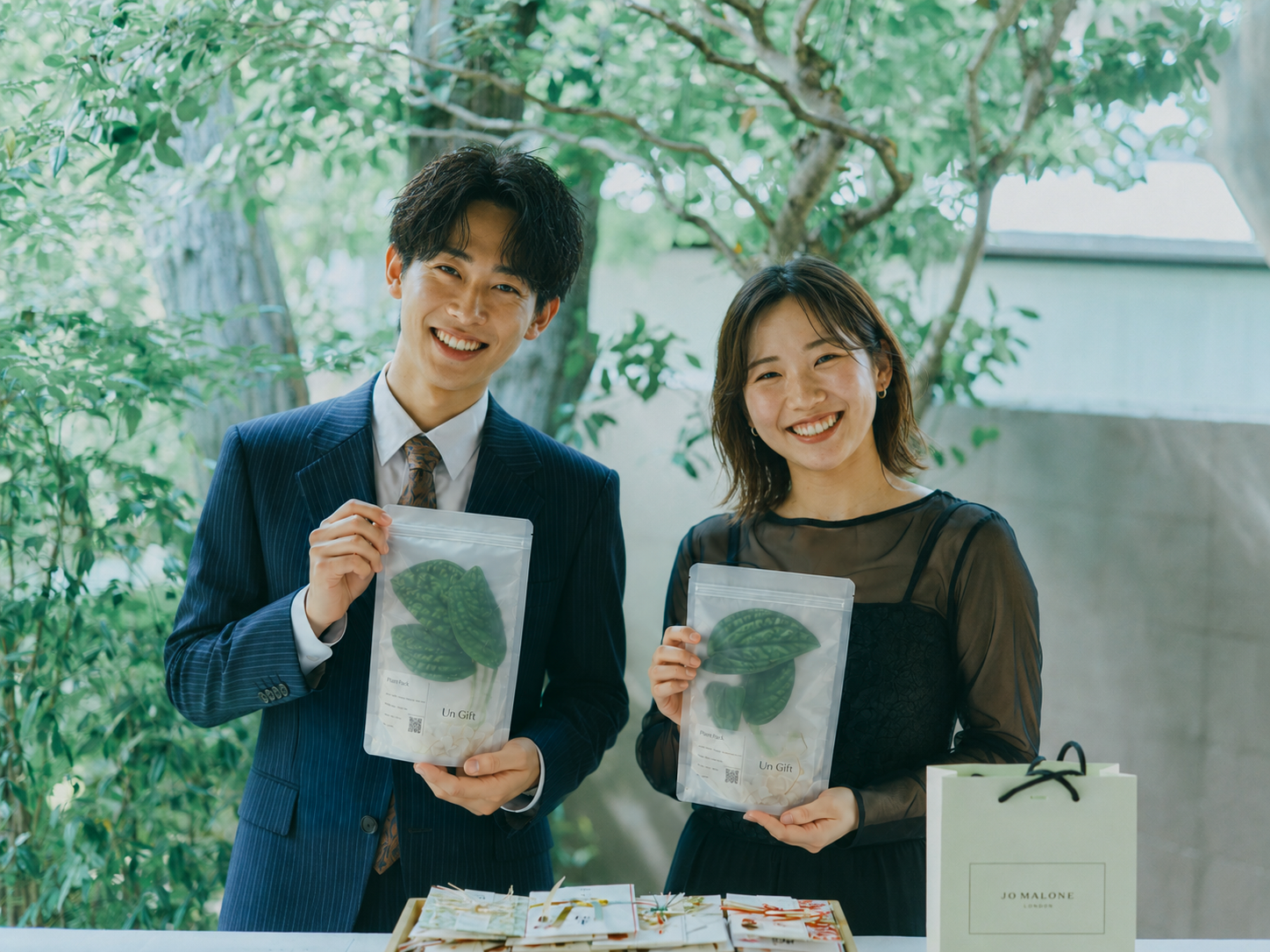 Un Giftの植物の引き出物を手にする、結婚式の装いのふたり